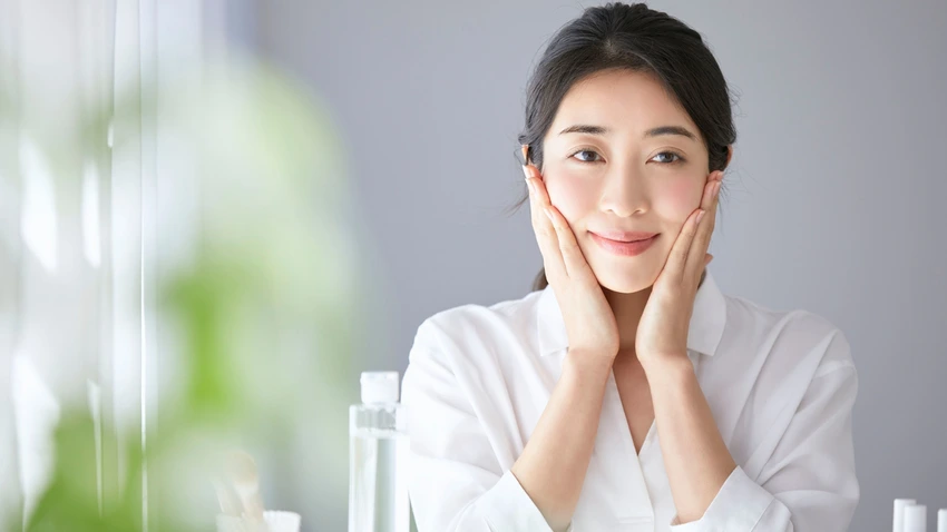両手で頬に触れ、潤いのある健やかな肌で微笑む女性